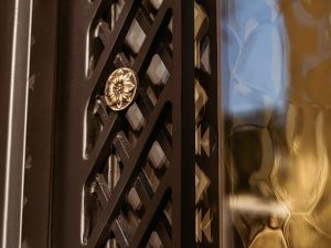 Close up image up custom wrought iron door with rippled glass, lattice iron work, and a floral ornament.